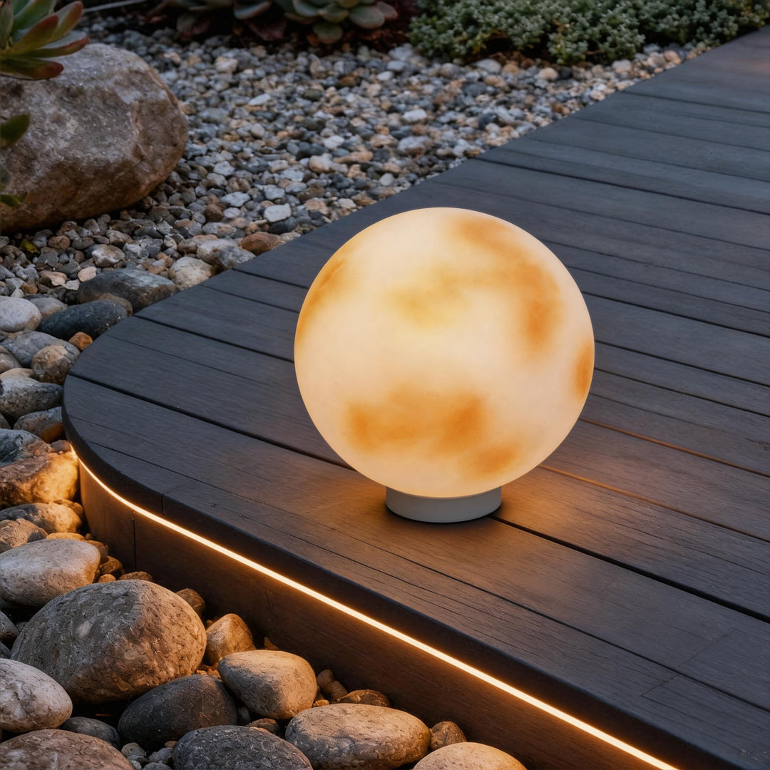 Moon-shaped stone pillar light on a dark timber deck with linear led lighting and river stones.