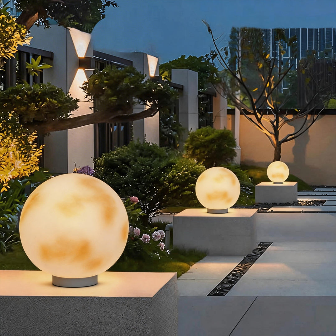 Multiple moon-shaped stone pillar lights lining a modern garden walkway during the blue hour ok.
