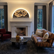 Mountain LED wall light mounted above a fireplace, glowing warmly in a modern living room.