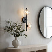 Multi light wall sconce mounted beside a mirror in a modern bathroom with soft ambient lighting.