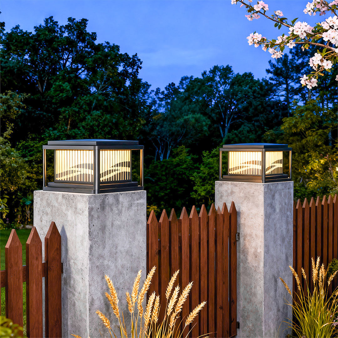 Multiple contemporary pillar lights mounted on concrete pillars with wood fence and landscaping at evening.