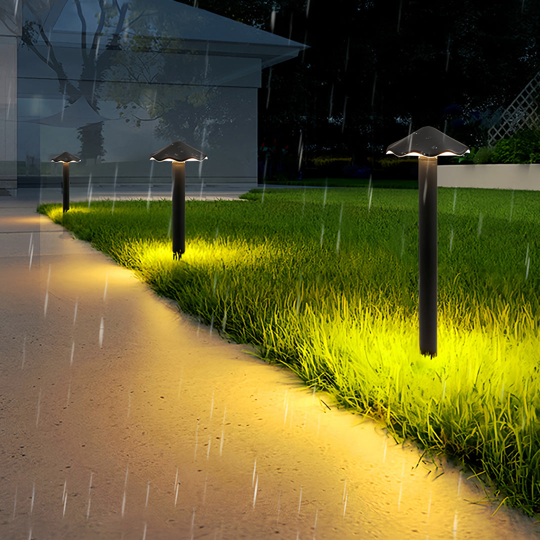 Multiple metal pathway lights providing warm, downward-facing light along a curving walkway in the rain.