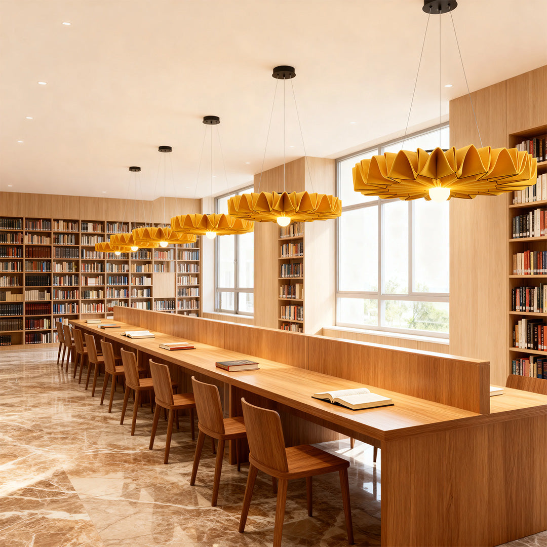 Multiple gold floral cloth chandeliers suspended over a long communal table in a library setting 