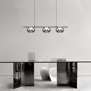 Multiple gray glass pendant lights creating ambient lighting in modern kitchen with black and white cabinetry.
