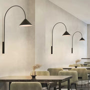Multiple wall arm lights with varying curved stems and cone shades illuminating modern cafe dining area.