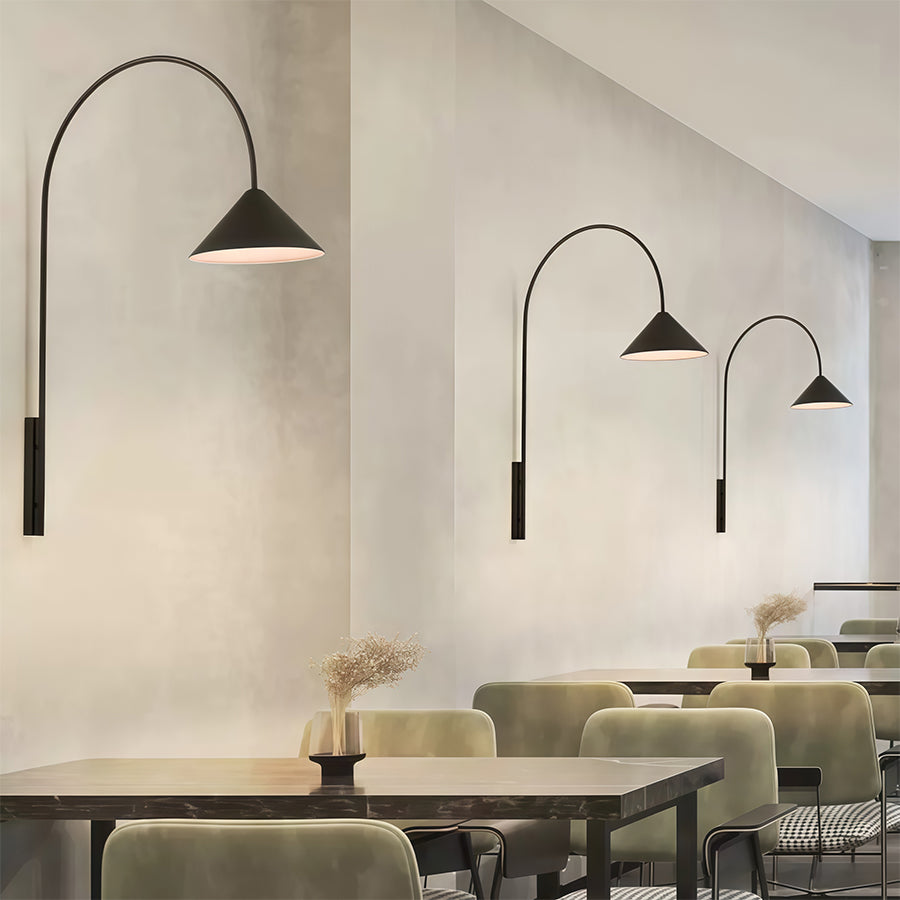 Multiple wall arm lights with varying curved stems and cone shades illuminating modern cafe dining area.