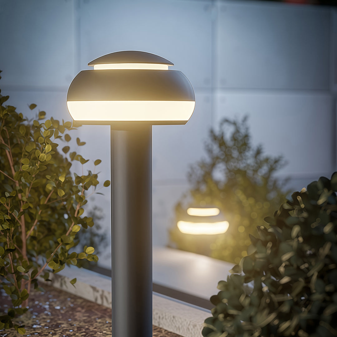 Mushroom path light in a garden with shrubs, adding a contemporary touch to the outdoor space.