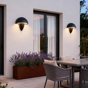 Mushroom-shaped wall light installed near plants in an outdoor setting, providing ambient lighting for the area.