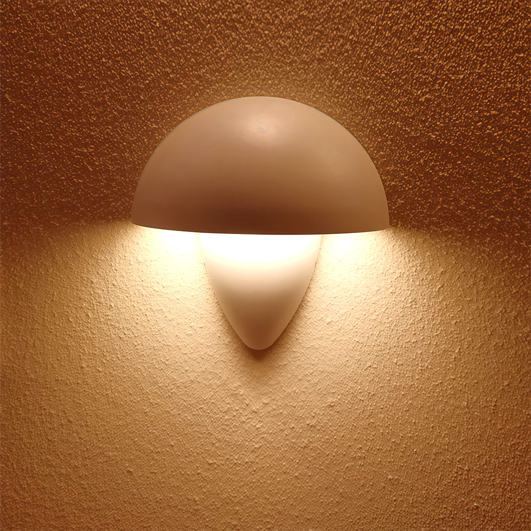 Mushroom-shaped white wall light illuminating a gray wall in an elegant outdoor setting, creating a stylish ambiance.