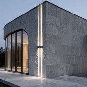 Minimalist narrow beam wall sconce creating focused vertical light lines on modern exterior wall.