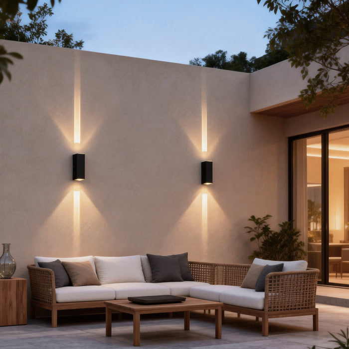 Modern narrow beam wall sconce illuminating an outdoor patio seating area, creating focused up and down lighting on a minimalist wall.