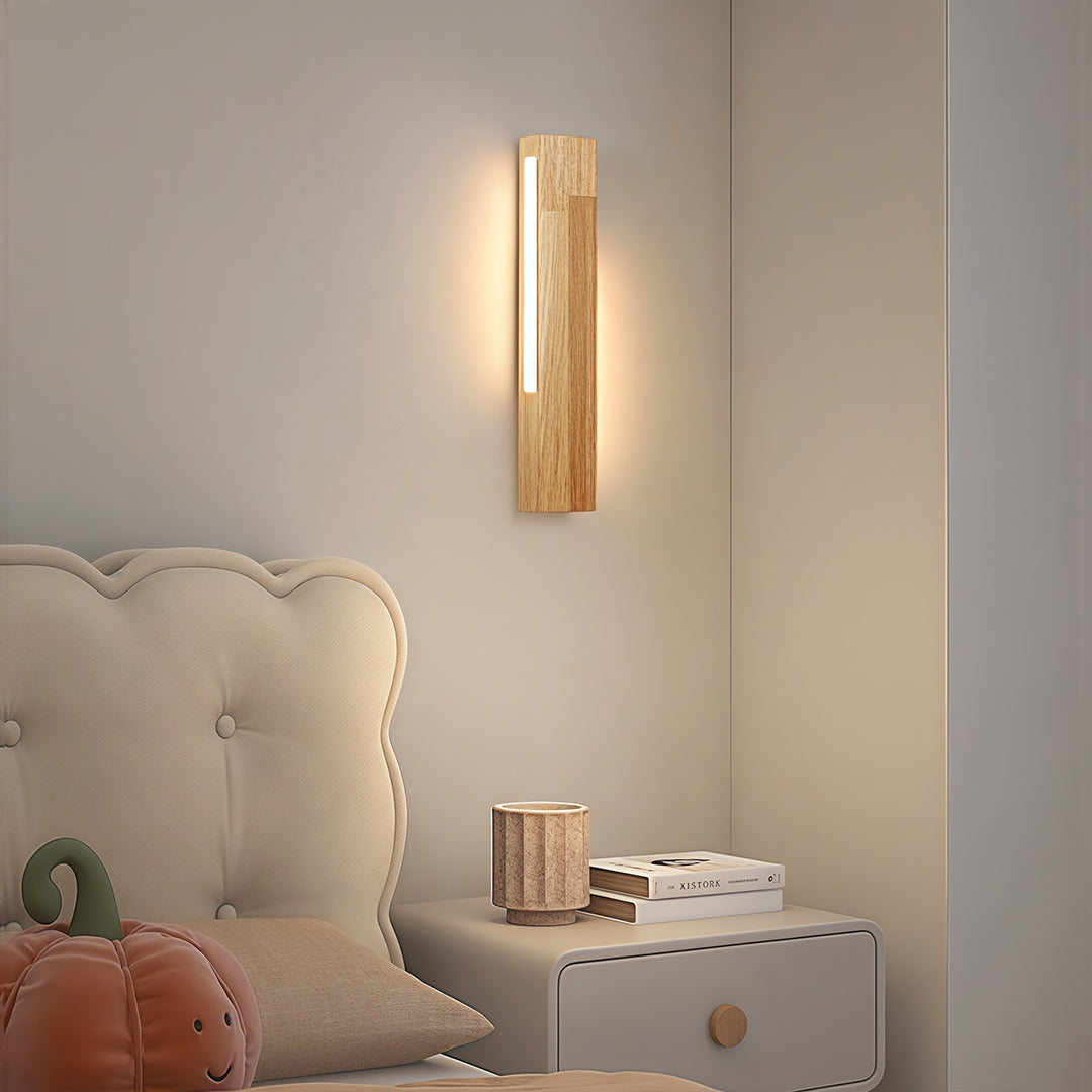 Light natural wood Japanese wall light fixture used as minimalist reading light beside a cozy upholstered headboard.