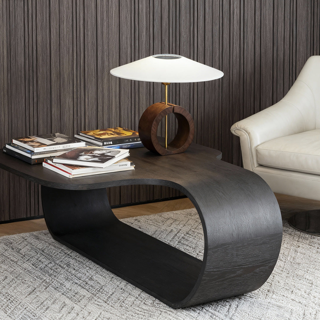 Modern natural wood table lamp next to reading chair and books on black console.