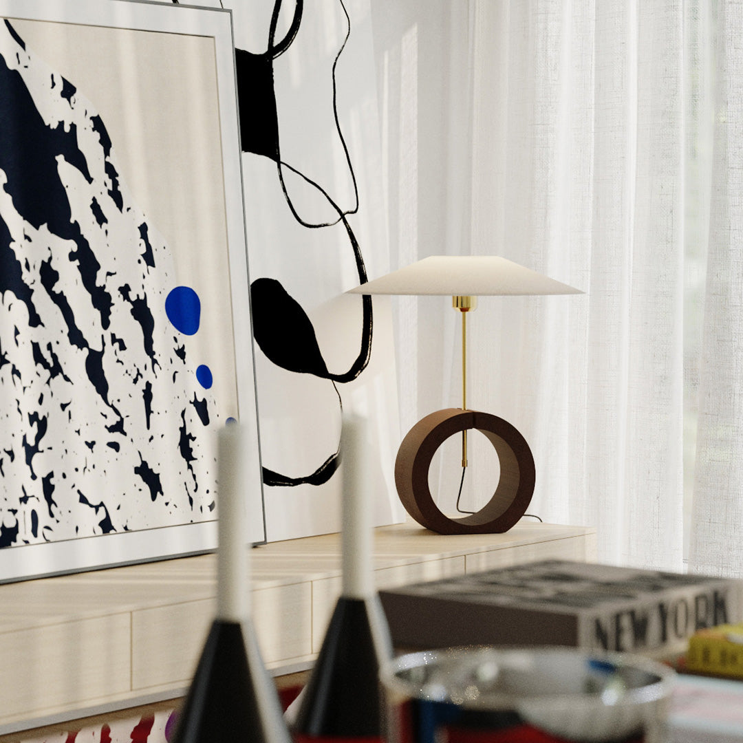 Round wood base table lamp with wide shade on beige sofa side table.