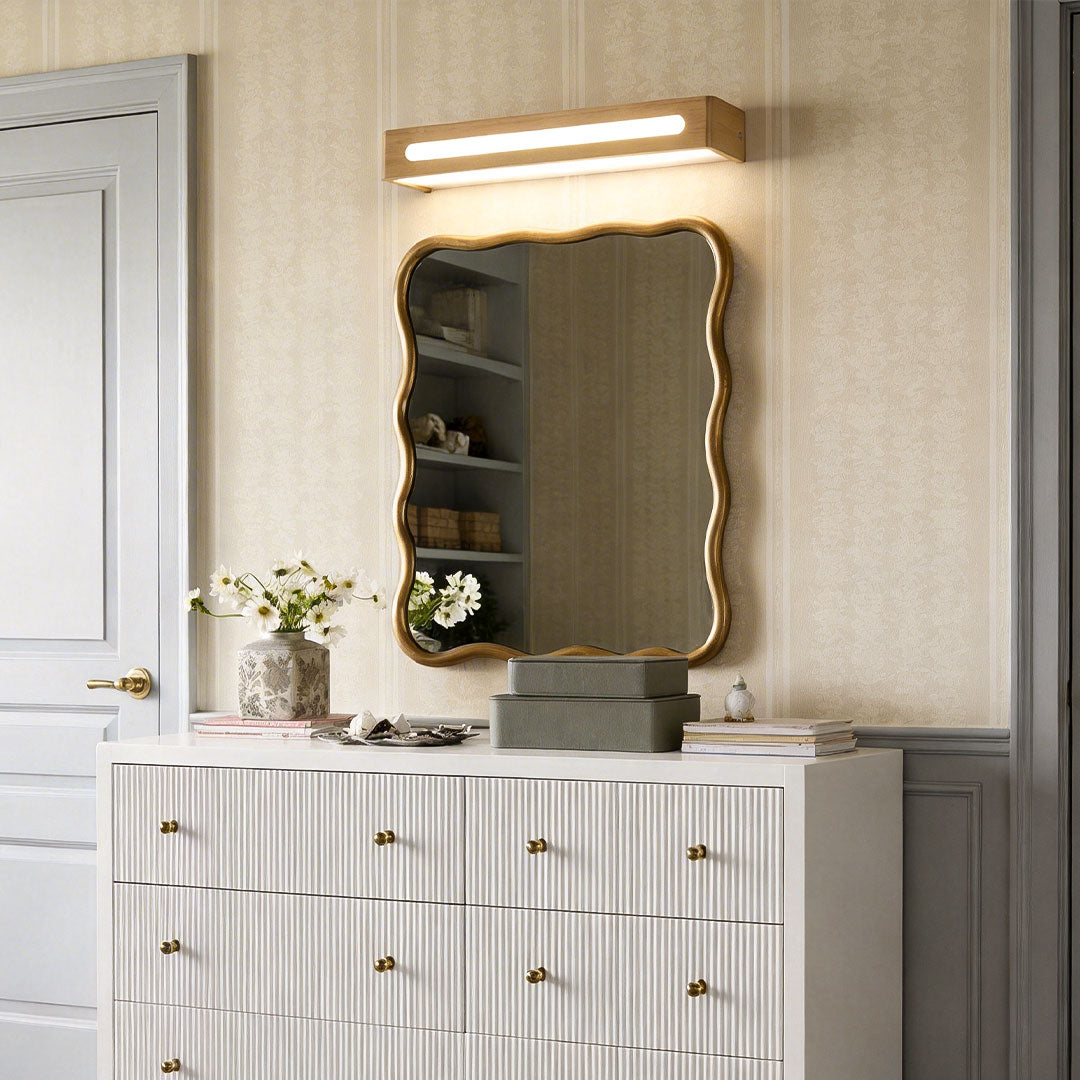 Oak wood vanity mirror light above a wavy gold mirror in bedroom decor.