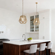 Single open-cage gold hanging pendant light suspended over a kitchen island with white cabinets and dark wood contrast.