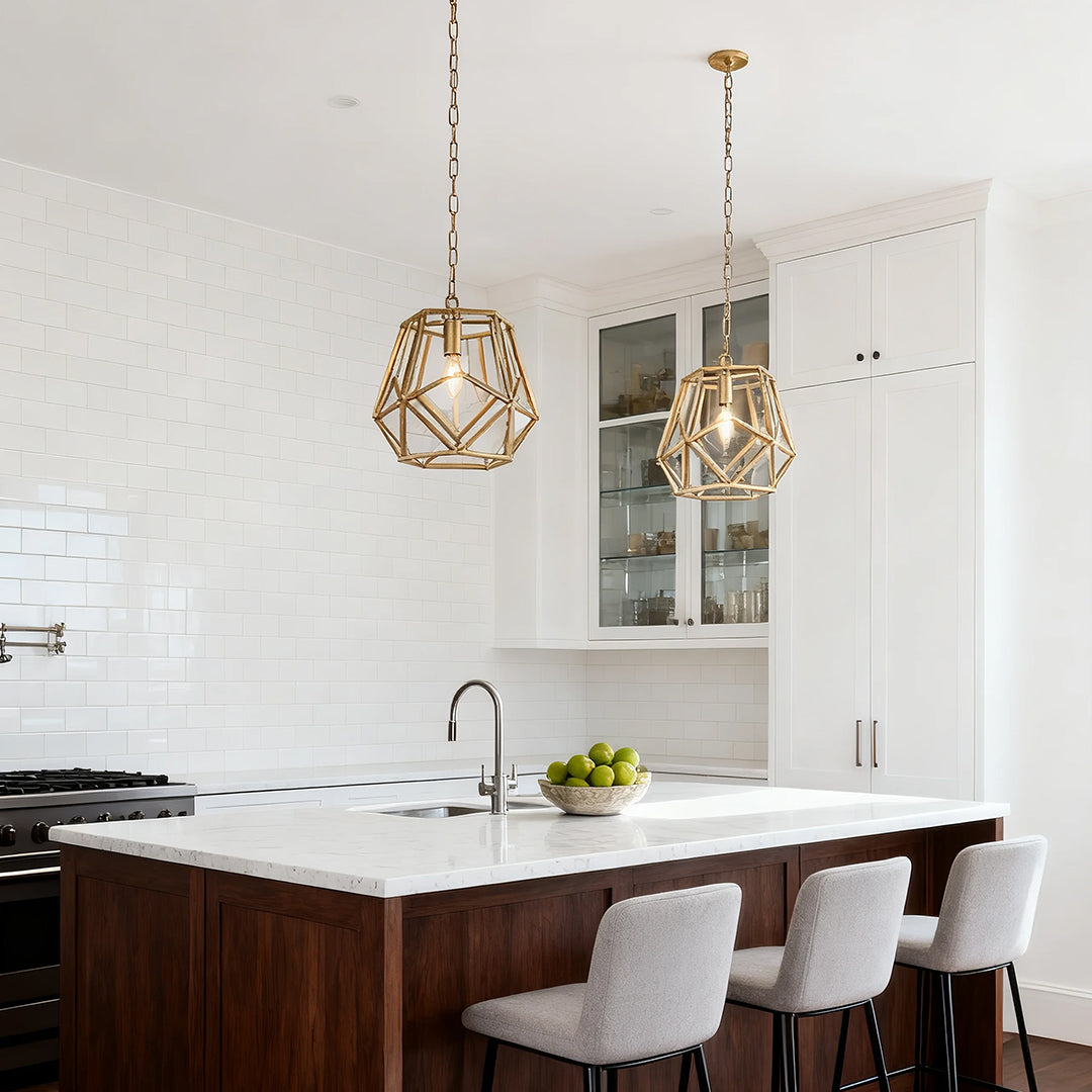 Single open-cage gold hanging pendant light suspended over a kitchen island with white cabinets and dark wood contrast.