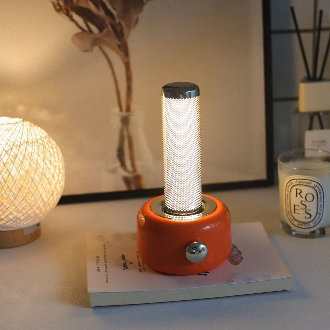 Orange industrial metal USB rechargeable table lamp providing warm ambient lighting on desk
