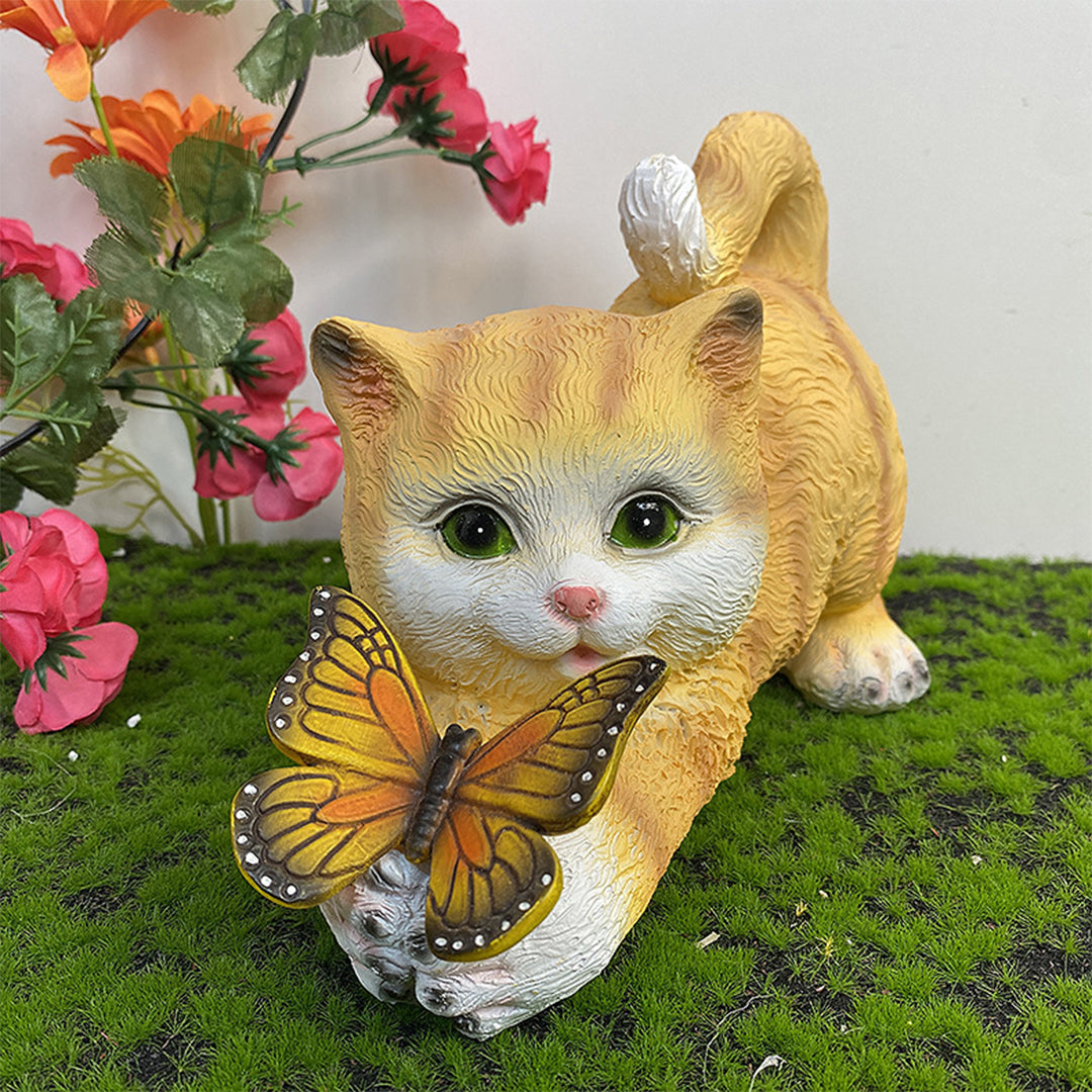 Orange kitten garden statue with illuminated butterfly among pink flowers and greenery