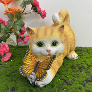 Orange kitten garden statue with illuminated butterfly among pink flowers and greenery