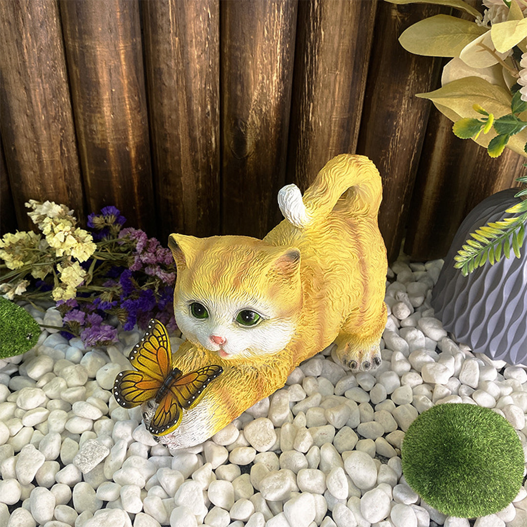 Orange kitten garden ornament with LED butterfly positioned among white pebbles and plants