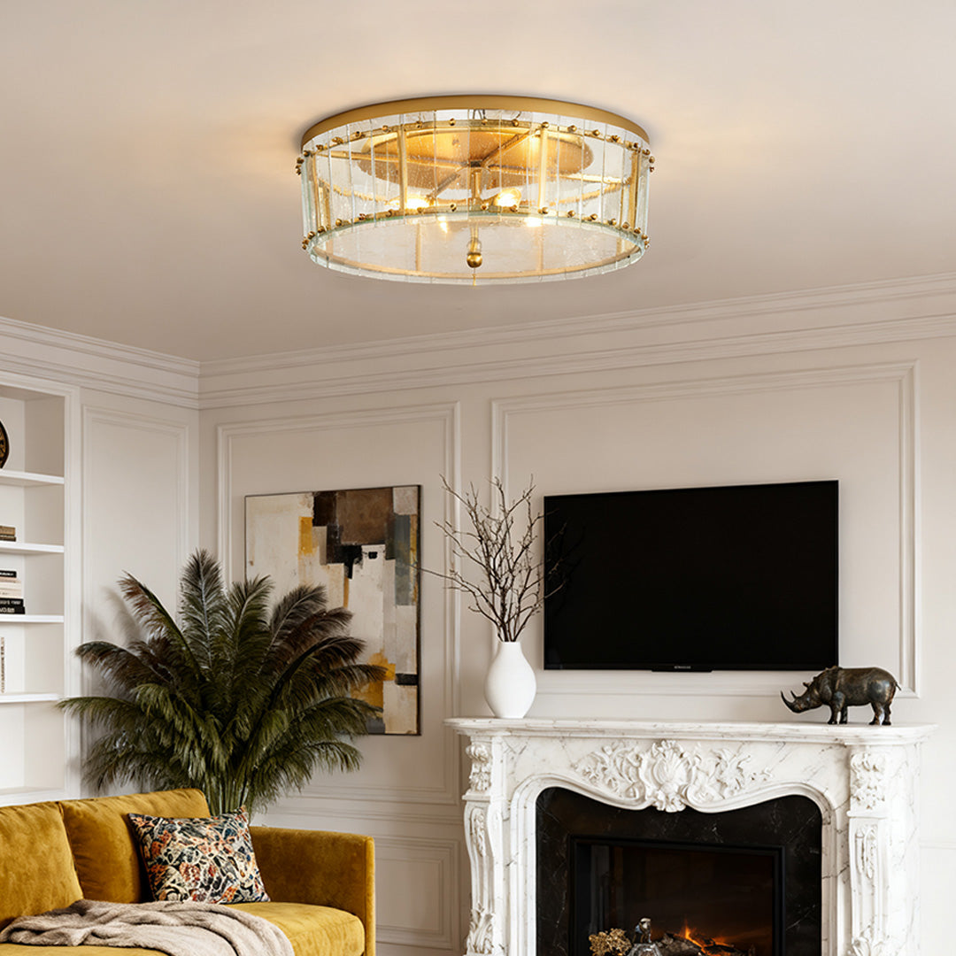 Ornate flush mount gold light with a crystal-trimmed glass drum shade, centered in a luxurious living room above a white marble fireplace.
