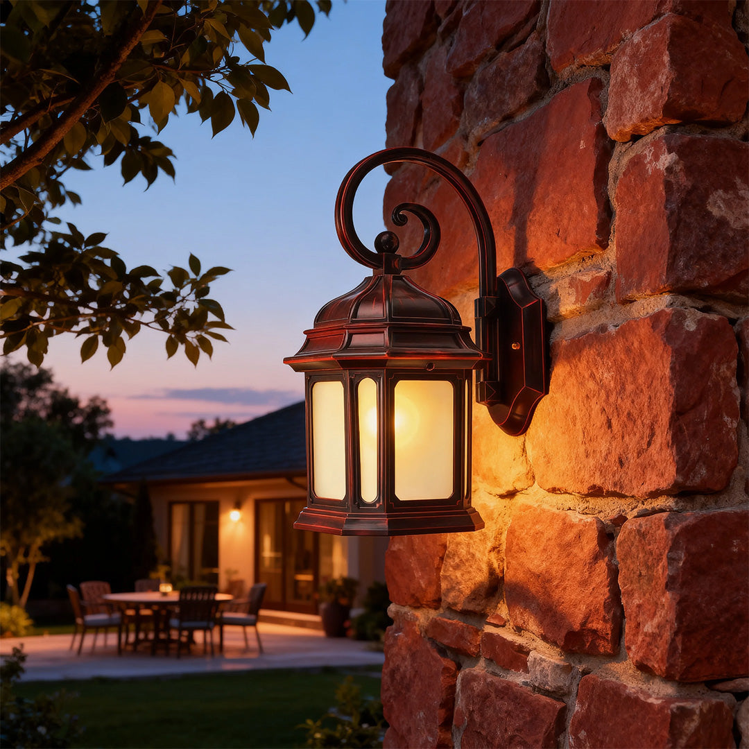 Ornate exterior LED wall light with scrollwork arm illuminating stone facade at dusk with building backdrop