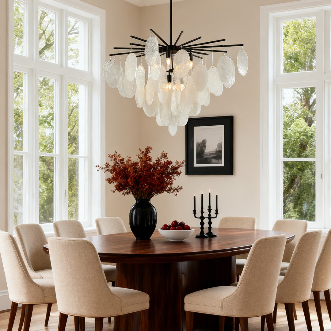 Ornate mother of pearl chandelier with leaf-like shell pieces, providing ambient light in a dining room with tall windows and classic molding.