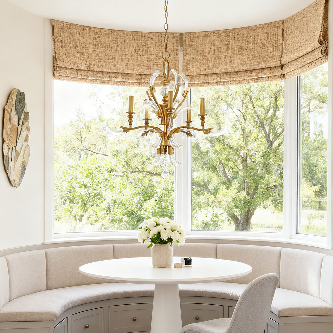Ornate gold and crystal chandelier with scrolling arms and floral glass accents, complementing a sophisticated kitchen and dining area with a long black table.