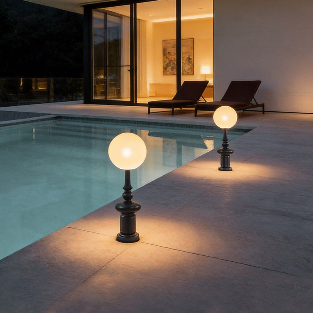 Outdoor black floor lamps with a modern spherical design, illuminating a poolside seating area.