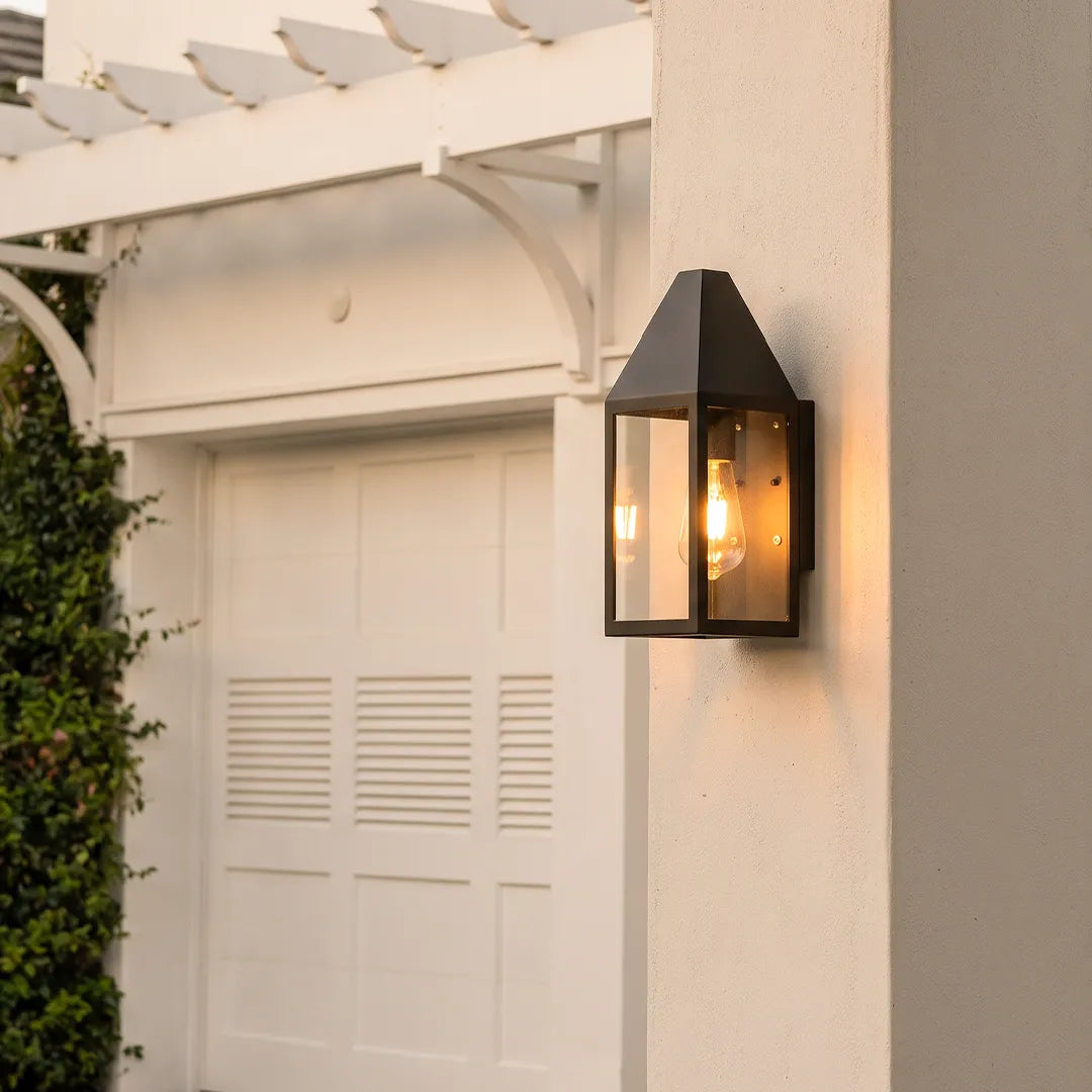 Outdoor black sconce mounted on a porch column, featuring a tapered lantern design with clear glass panels.