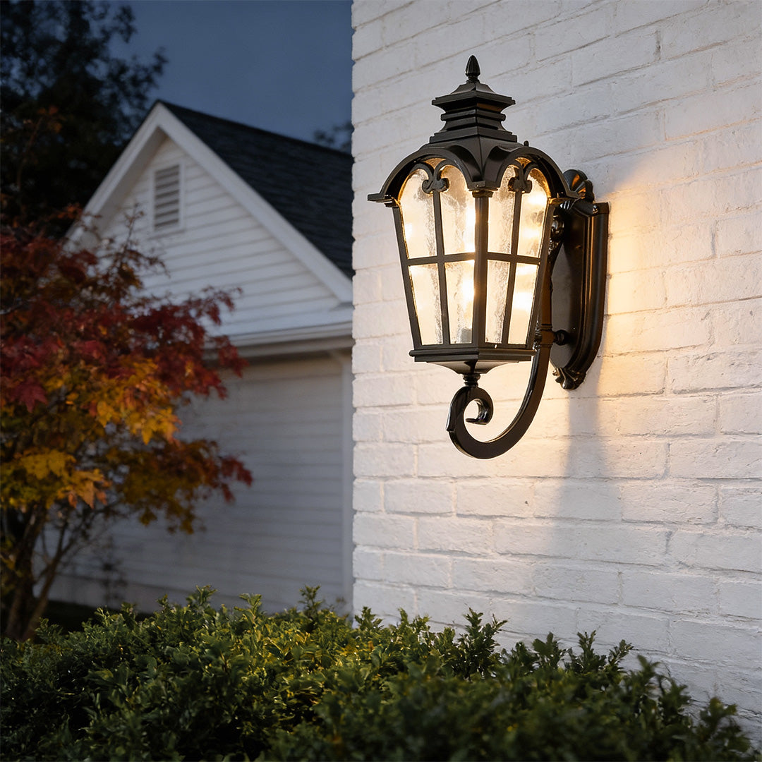 Outdoor black sconce mounted on a white wall, providing elegant illumination near a garden entrance.