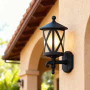 Close-up outdoor black wall light with crisscross design illuminating cream-colored stucco entrance wall