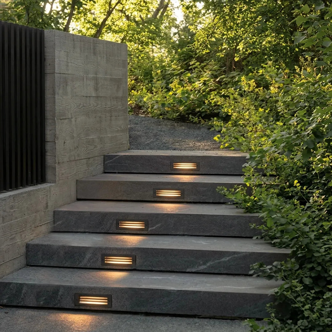 Outdoor brick light installed on modern concrete garden steps, casting a warm glow along the stair pathway.
