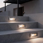 Outdoor brick light embedded in modern stone stair risers, providing subtle step illumination for a contemporary residential exterior.