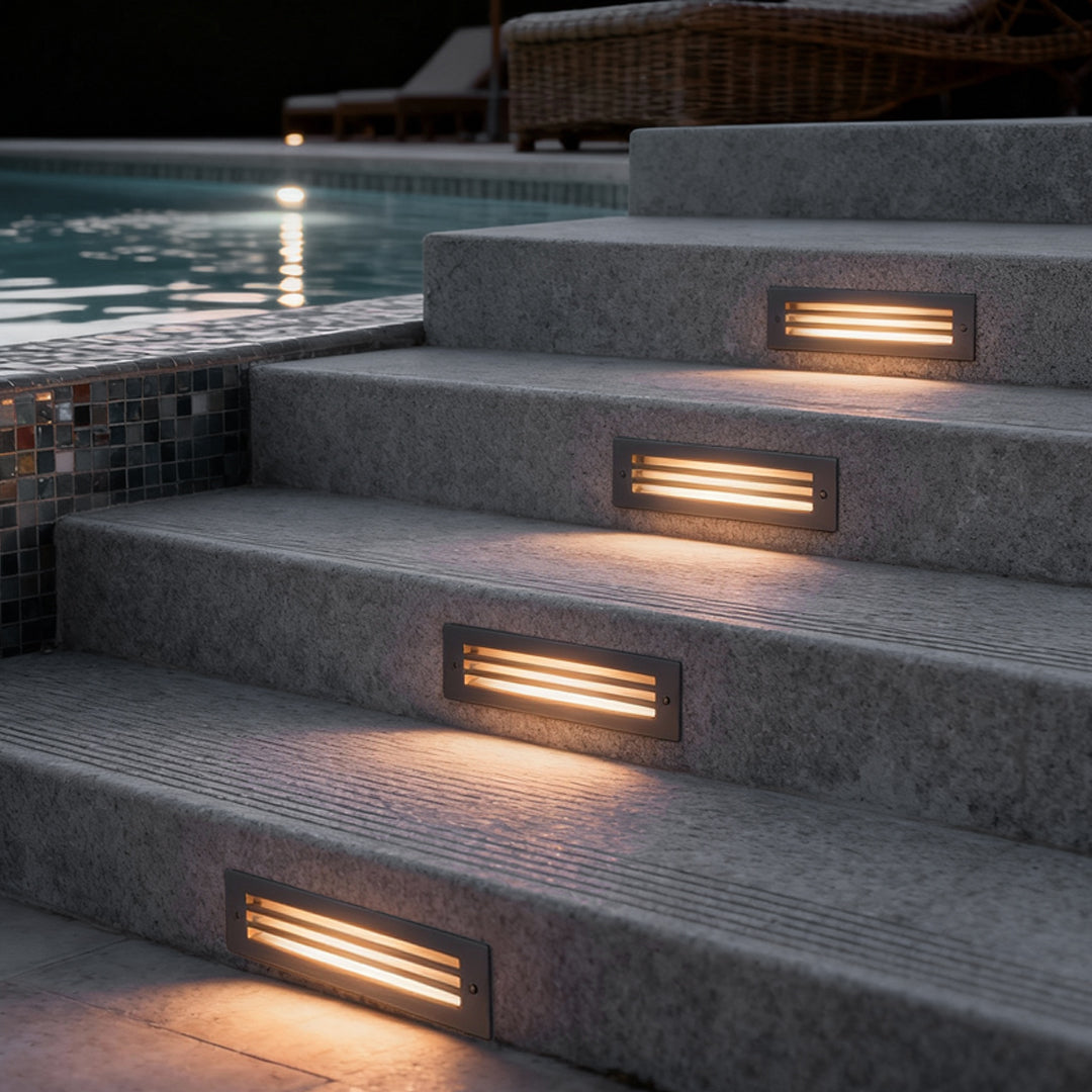 Outdoor brick light installed on concrete poolside steps, emitting warm horizontal light to improve safety and create a modern night ambiance.