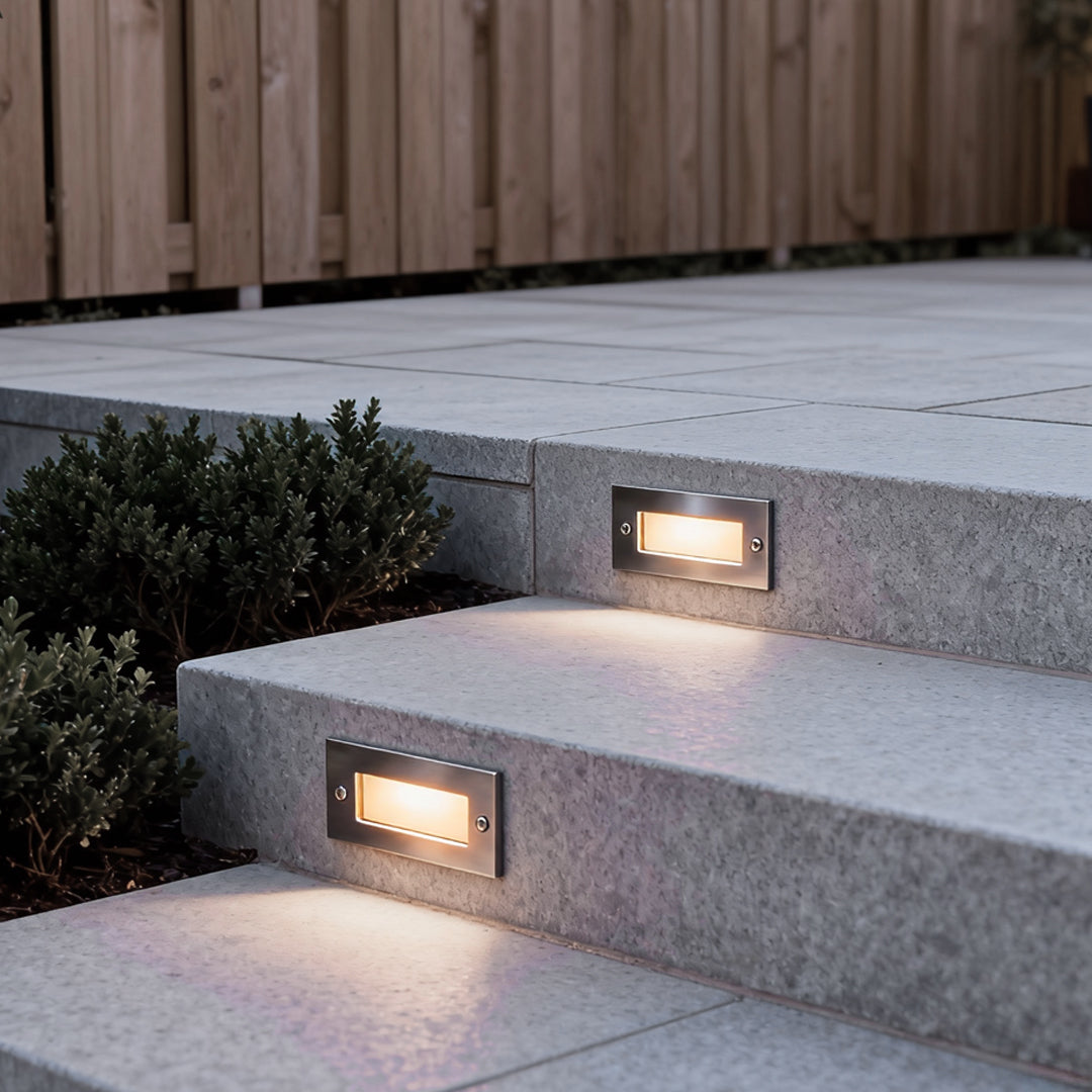 Outdoor brick light recessed into gray outdoor steps near landscaping, offering low-glare lighting for pathways and elevation changes.