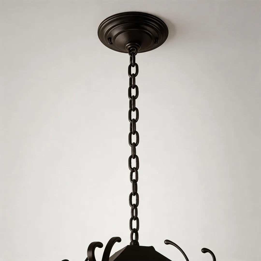 Outdoor ceiling pendant light detail showing the dark metal canopy, hanging chain, and decorative top scroll accents.