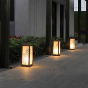 Warm glowing bollard lighting fixtures placed along an outdoor walkway in a landscaped garden.
