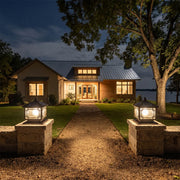 Outdoor garden pillar lights illuminating a front walkway with stone columns and a landscaped lawn at night.