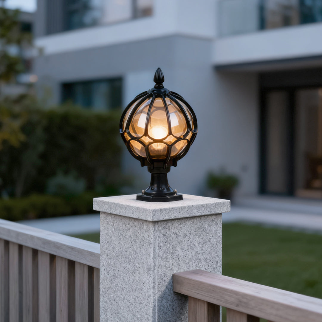 Outdoor globe pillar light installed on a stone fence post, emitting warm ambient light in a modern residential setting.
