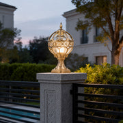 Outdoor globe pillar lights with intricate gold metalwork, mounted on a stone pillar near a modern house entrance.