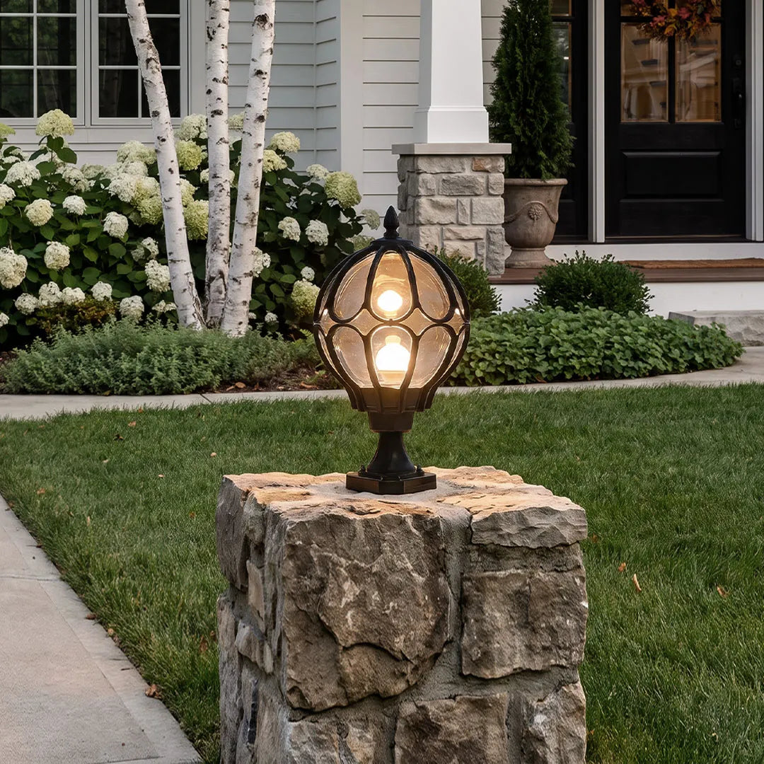 Outdoor globe pillar lights mounted on a stone entry column beside a front lawn and walkway.