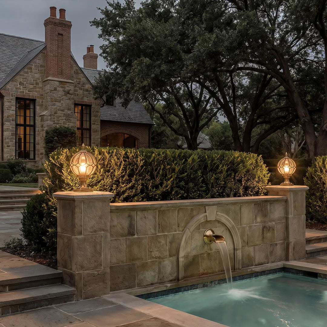 Outdoor globe pillar lights illuminating a stone garden wall and poolside steps at dusk.