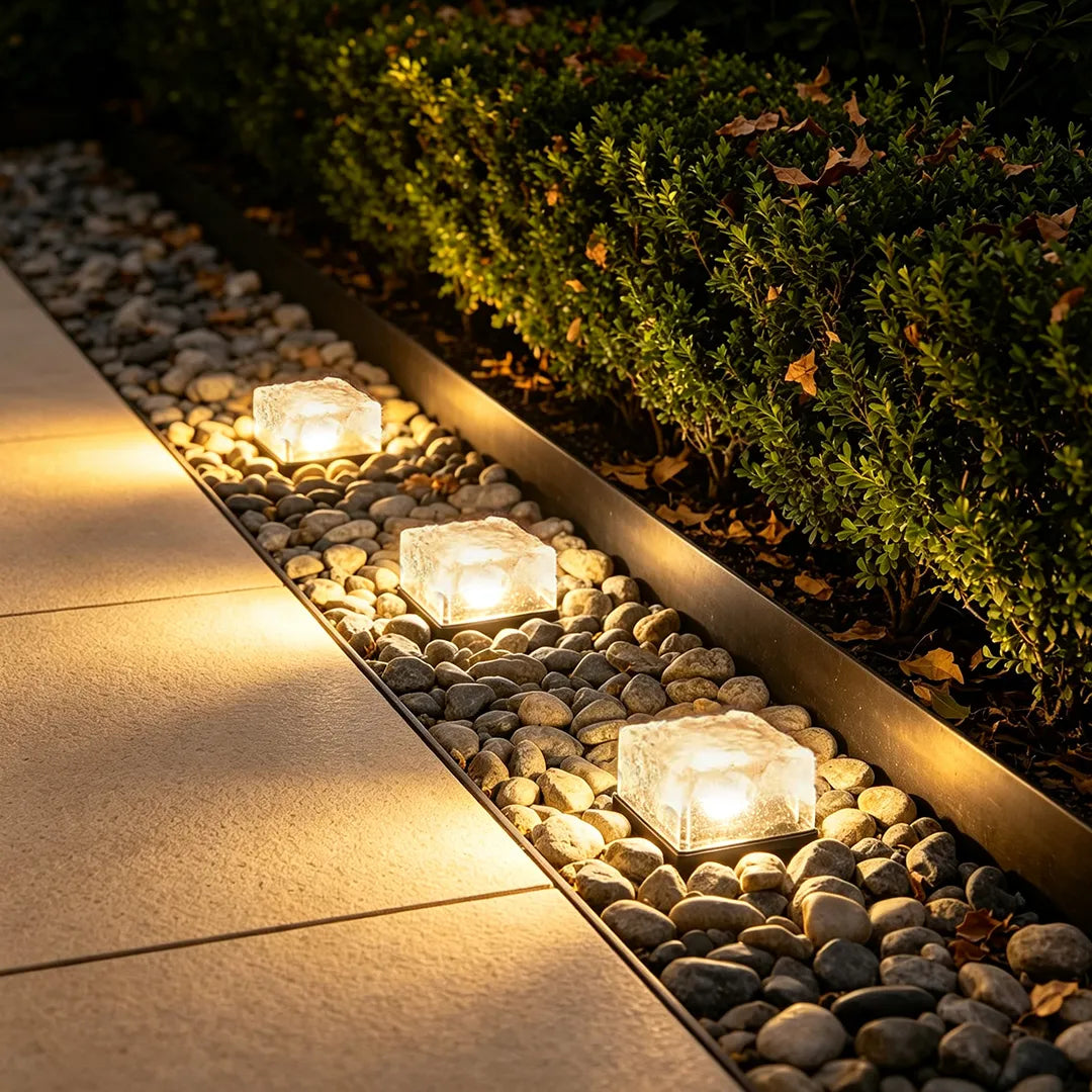 Outdoor ice cube lights installed beside a garden border, illuminating pebbles and shrubs with a warm glow.