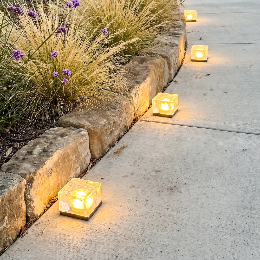 Outdoor ice cube lights placed along a stone-edged walkway, adding a warm decorative glow to the garden path.