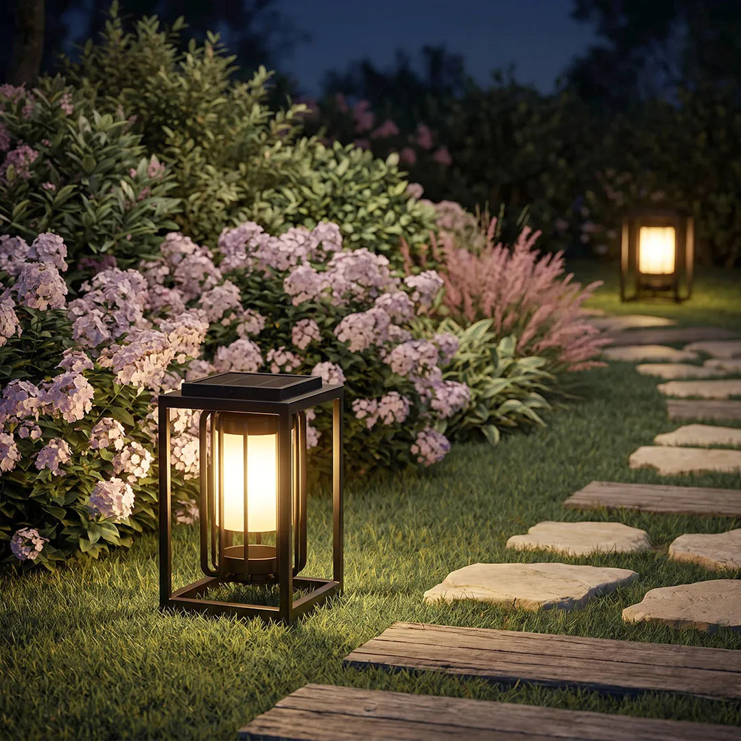 Outdoor lantern light fixture illuminating a garden path beside blooming flowers and stepping stones at night.