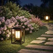 Outdoor lantern light fixture illuminating a garden path beside blooming flowers and stepping stones at night.