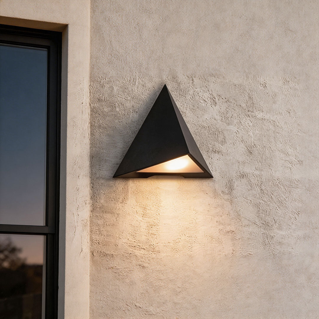 Outdoor LED wall sconce with a modern triangular design, mounted on a light gray exterior wall.