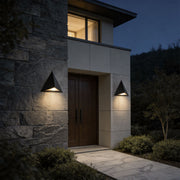 Outdoor LED wall sconce with a modern triangular design, providing warm illumination near an entrance.
